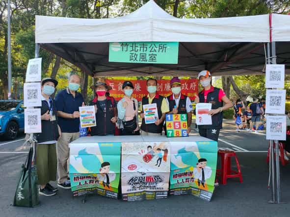 新竹縣政府政風處廉政志工協助竹北市公所政風室辦理「2022竹北趣遊親子路跑  全家大小反貪反賄選樂遊趣」設攤宣導活動竹北市公所政風室同仁與廉政志工於宣導攤位前合影