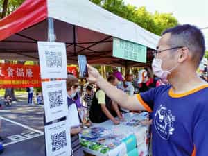 新竹縣政府政風處廉政志工協助竹北市公所政風室辦理「2022竹北趣遊親子路跑  全家大小反貪反賄選樂遊趣」設攤宣導活動民眾掃描QRCode觀看反賄選影片